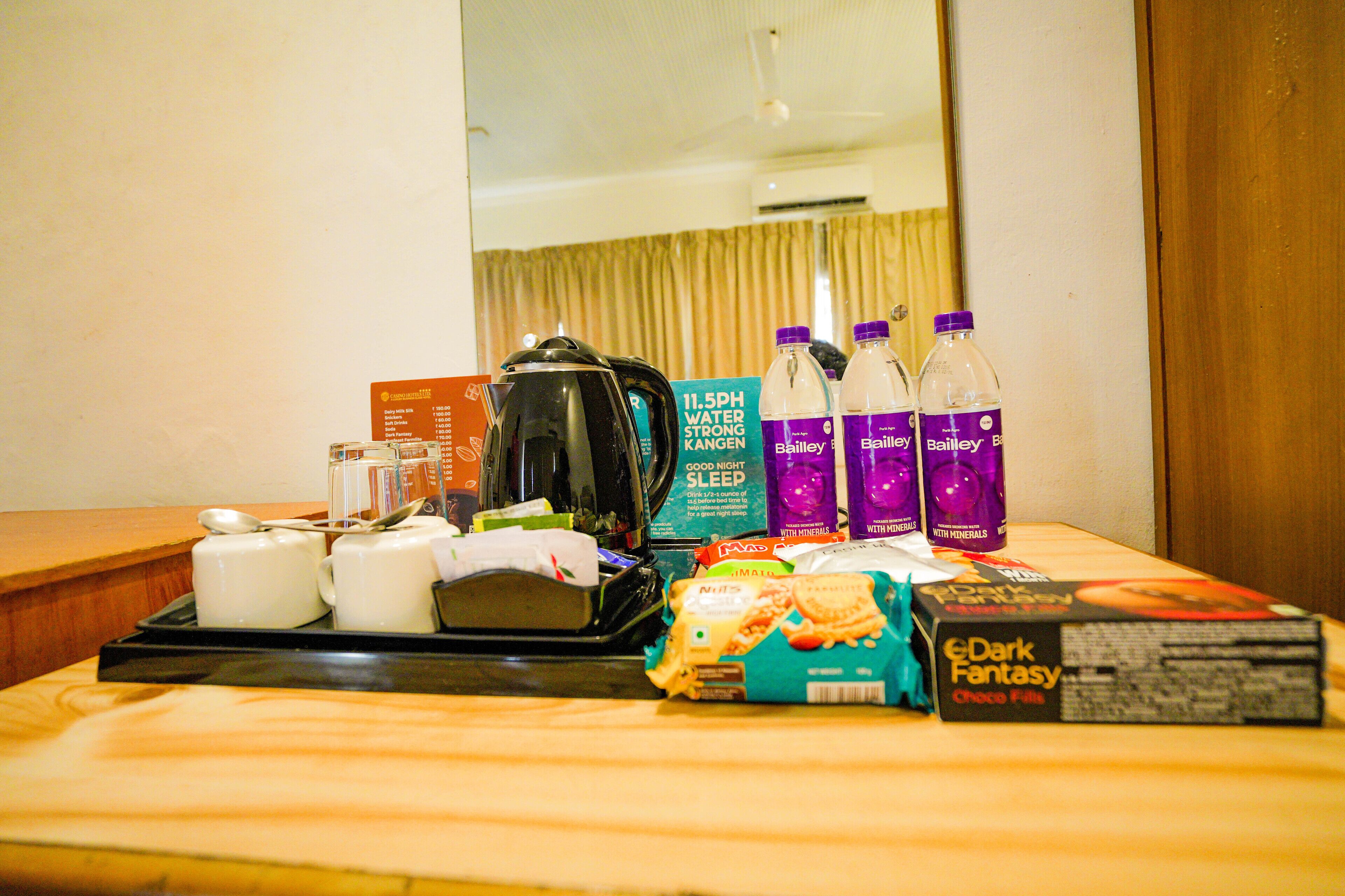 Habitación de hotel con una mesa dispuesta con tazas de té, una tetera, botellas de agua Bailey's, una caja de Bailey's y una caja de Dark Fantasy Choco Fills.