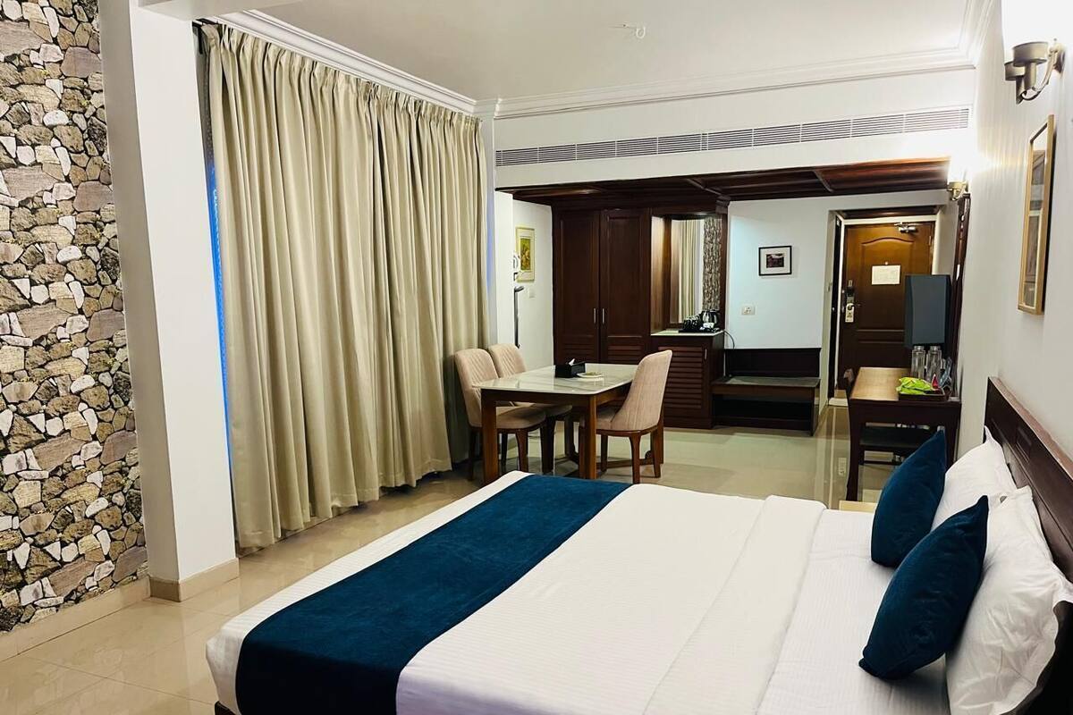 Une chambre d’hôtel avec un grand lit, un bureau et une chaise. Un mur en pierre et un rideau se trouvent sur un des côtés.