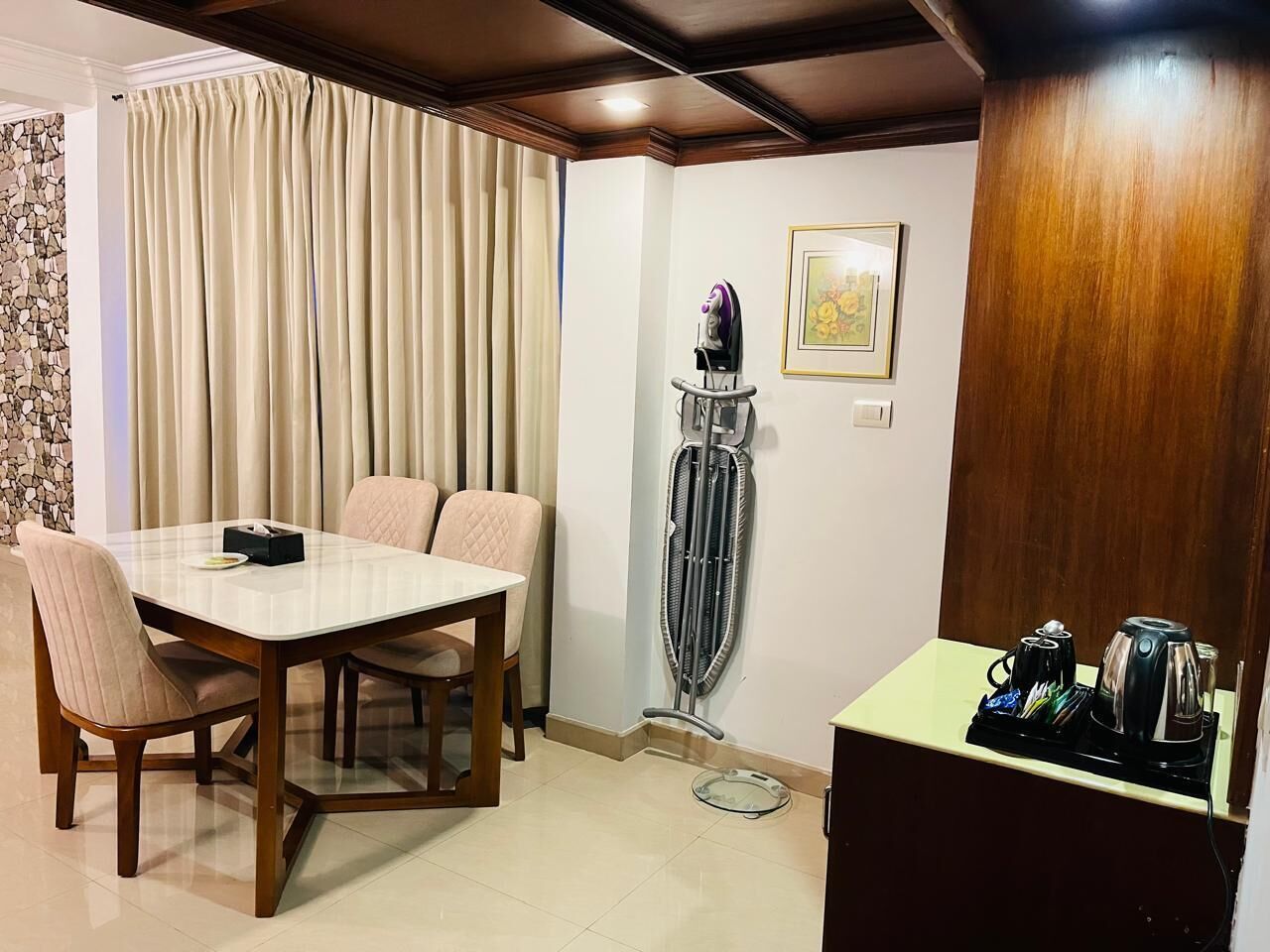 A dining area with a table and chairs, a standing heater, a coffee maker, and a small cabinet.