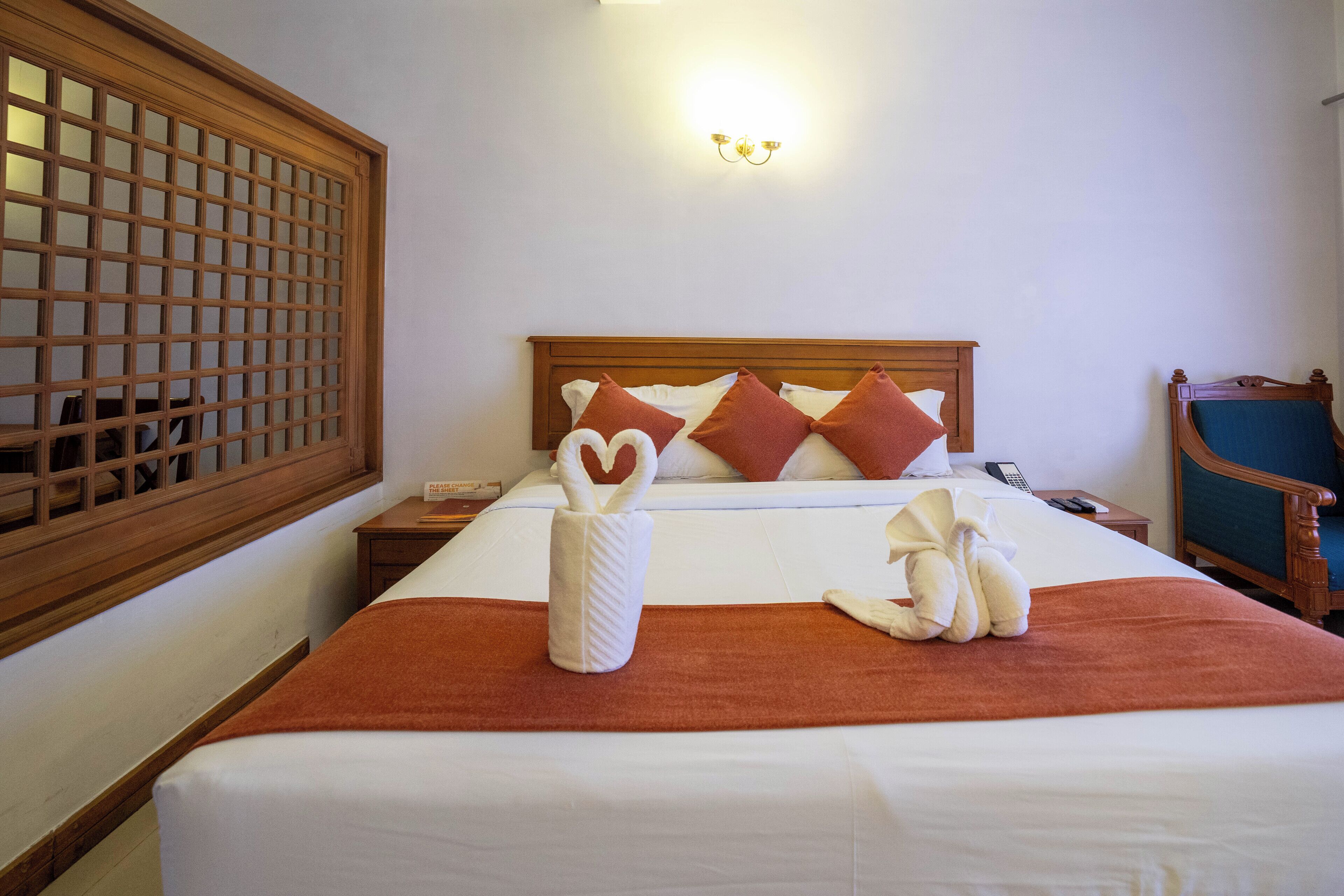 Una cama bien hecha con un edredón marrón, dos toallas dobladas en forma de cisnes y un cabecero de madera.