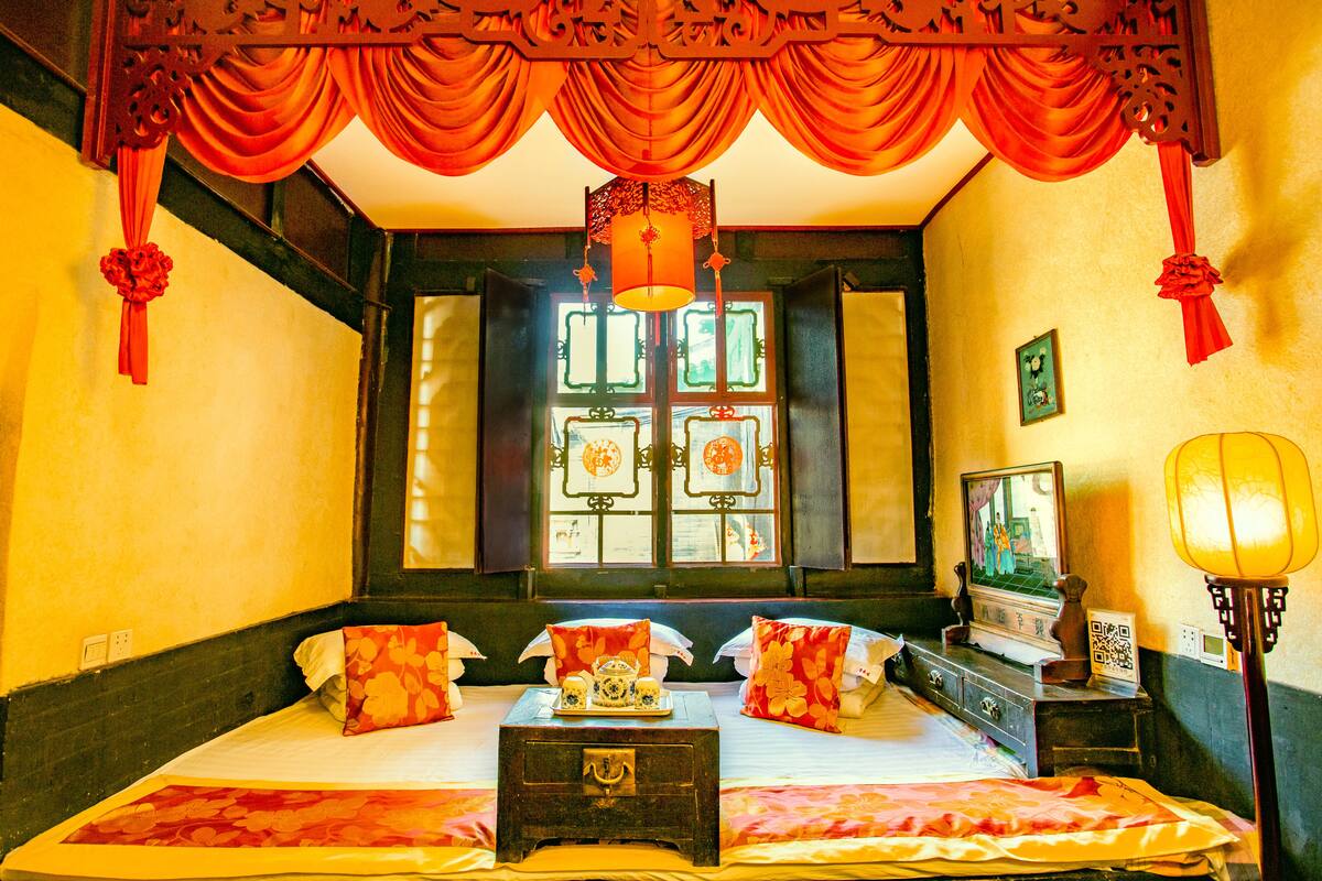 A traditional room with a bed, a chest of drawers, a table with a tray, and a window with decorative panes.