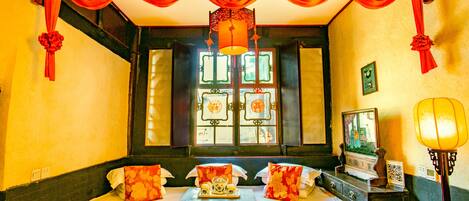 A traditional room with a bed, a chest of drawers, a table with a tray, and a window with decorative panes.