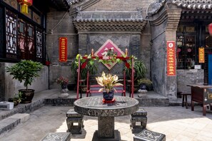 A courtyard with a traditional Chinese-style table and chairs, surrounded by potted plants and a decorative archway. - Pingyao Ji Family Courtyard Inn (Jinzhong)