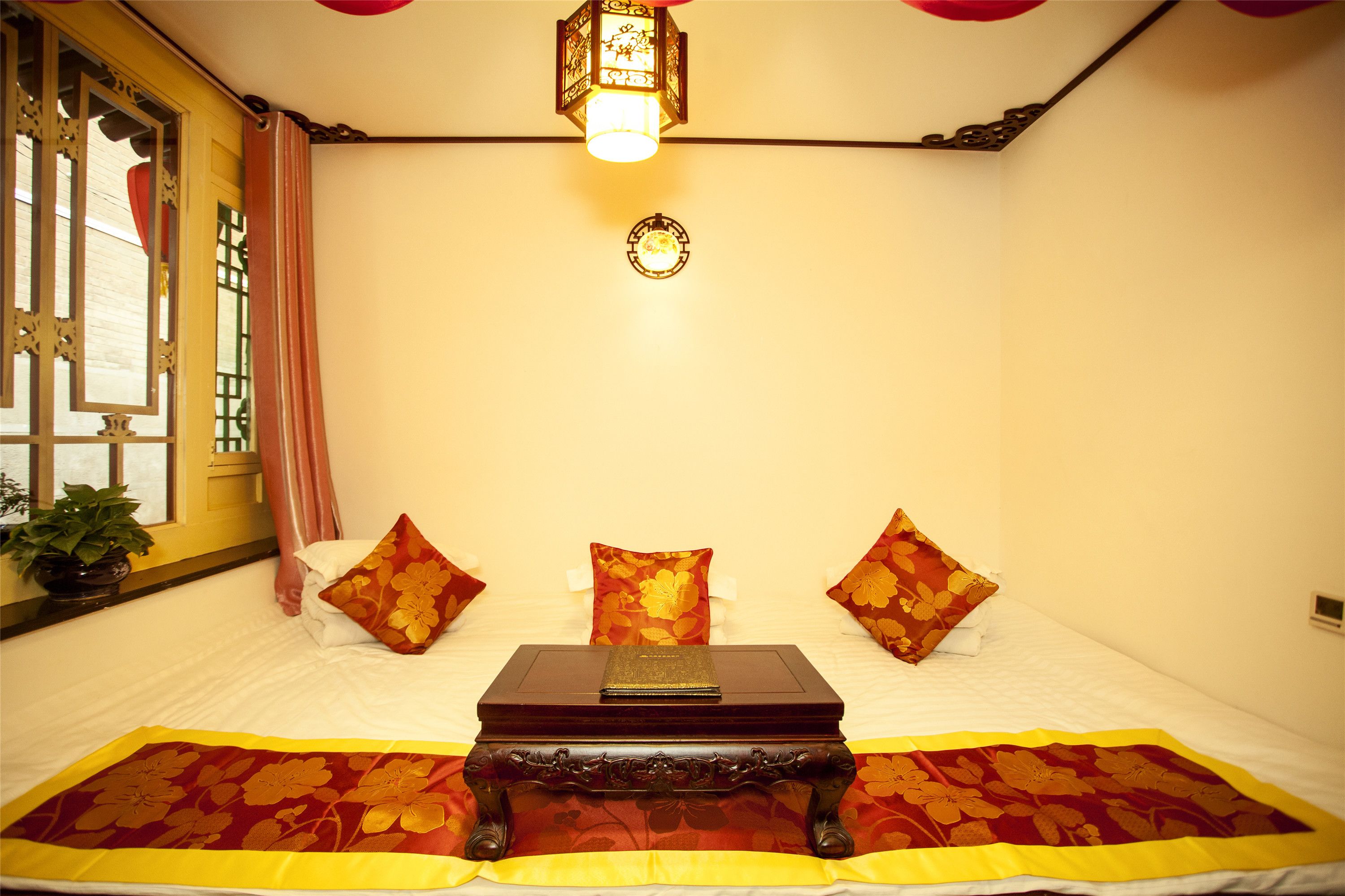 A neatly made bed with floral pillows, a bedside table with a book, and a traditional lantern.