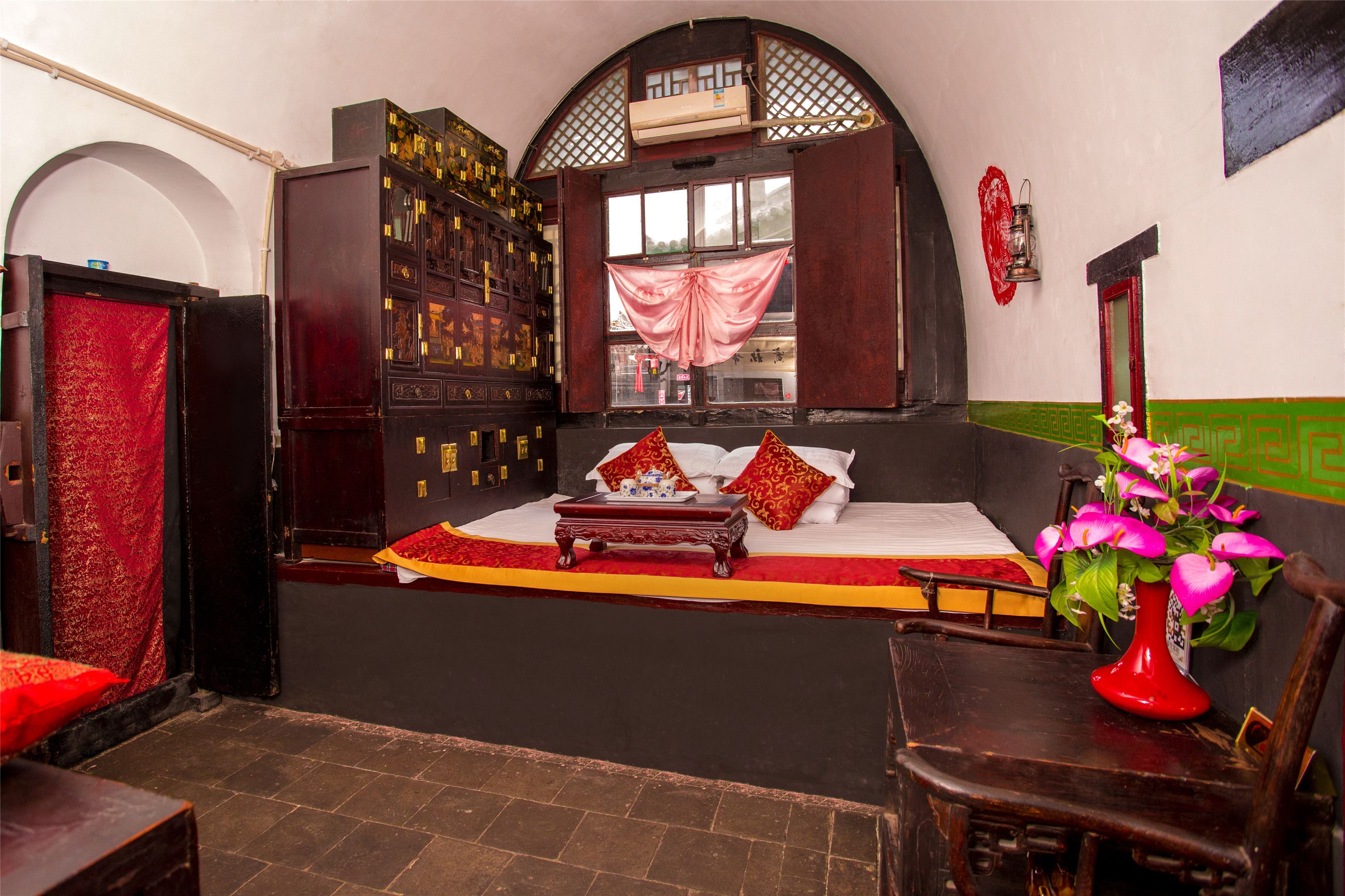 A traditional room with a bed, a wooden cabinet, a red curtain, and a vase with flowers.