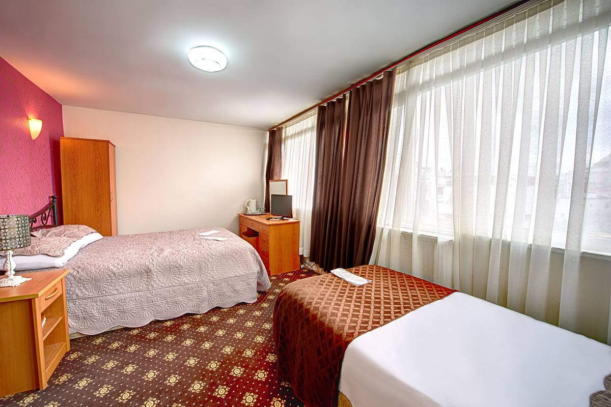 A hotel room with two beds, a desk, a wardrobe, and a window with curtains.