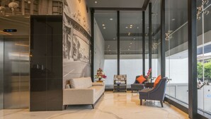 A modern lobby with a sofa, armchairs, a small table with flowers, and a large window offering a view of the outdoors. - Hotel 88 Kedungsari by WH (Surabaya)