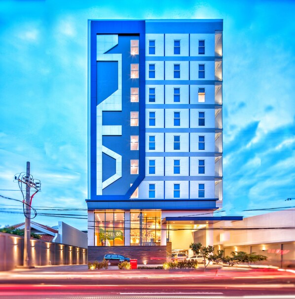 Un hotel moderno con una fachada geométrica distintiva, varios pisos y una entrada a nivel de calle con estacionamiento visible.