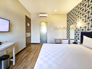 Habitación de hotel con cama, escritorio y armario. Tiene un televisor montado en la pared y un equipo de aire acondicionado.