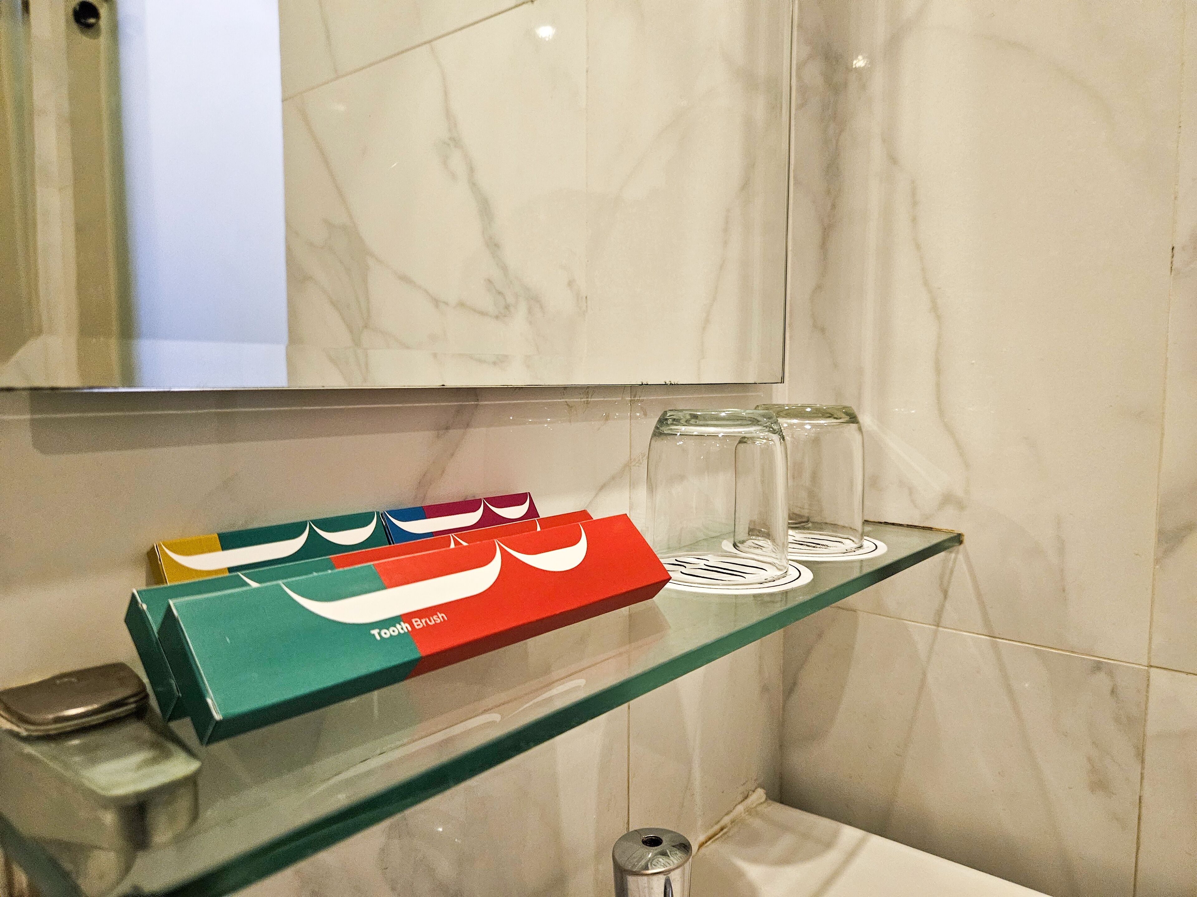 Un baño con un estante de vidrio que sostiene cepillos de dientes y un recipiente de vidrio.