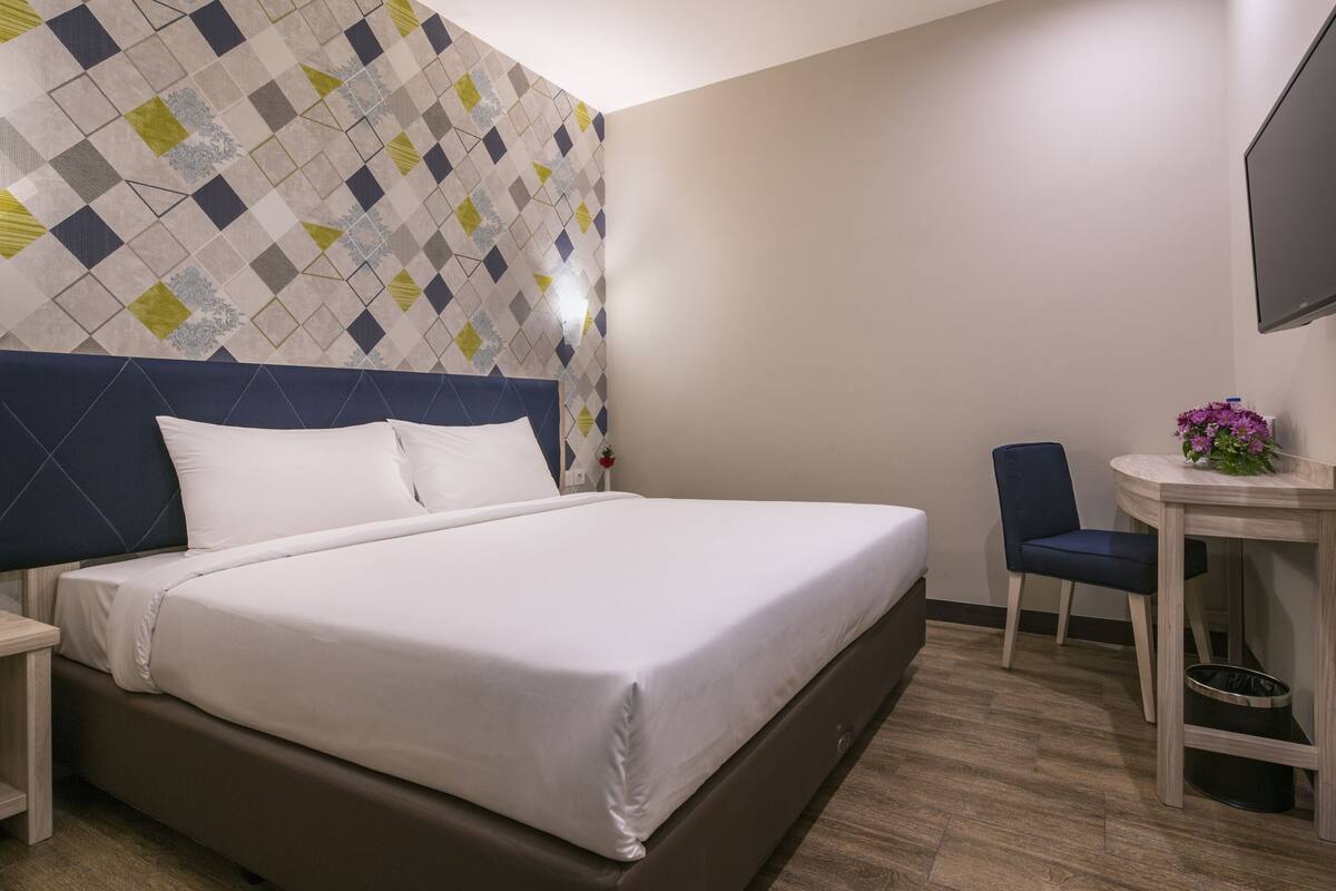 Hotellihuone, jossa on suuri sänky, työpöytä tuolilla sekä seinälle asennettu televisio.