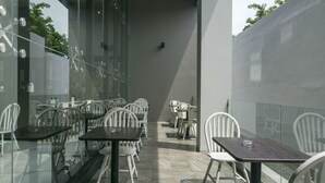 An outdoor dining area with glass walls, white chairs, and tables. - Hotel 88 Kedungsari by WH (Surabaya)