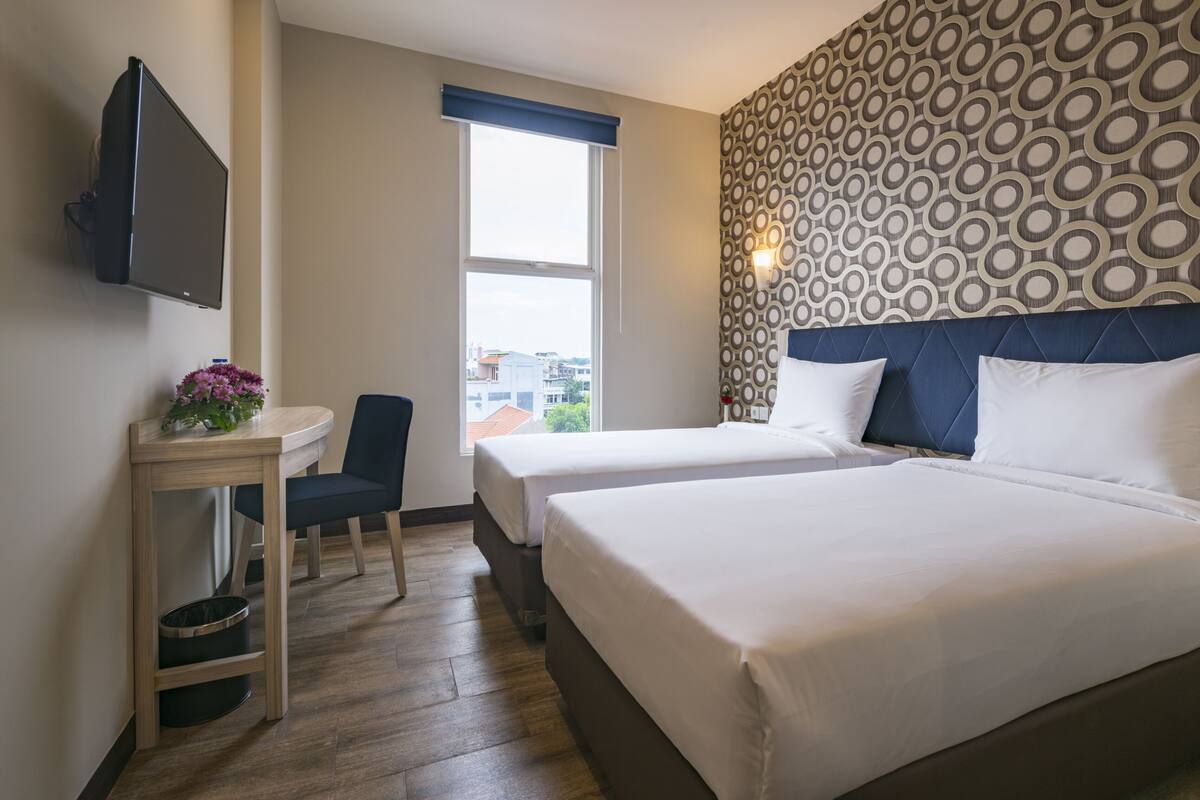 Hotellihuone, jossa on kaksi sänkyä, työpöytä, tuoli, televisio ja kuviollinen seinä.