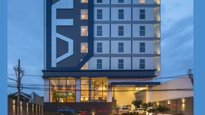A modern hotel with a prominent geometric facade, multiple floors, and a ground-level entrance with a visible sign. - Hotel 88 Kedungsari by WH (Surabaya)