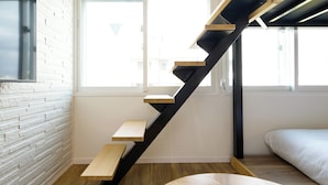 Una escalera moderna con escalones de madera y barandillas de metal negro, que conduce a un dormitorio con cama y ventana.