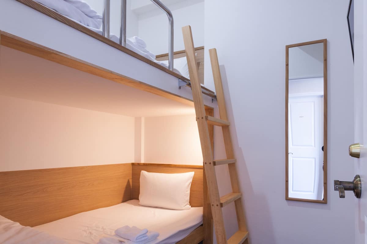 A bunk bed with a wooden ladder, a white door, and a mirror on the wall.