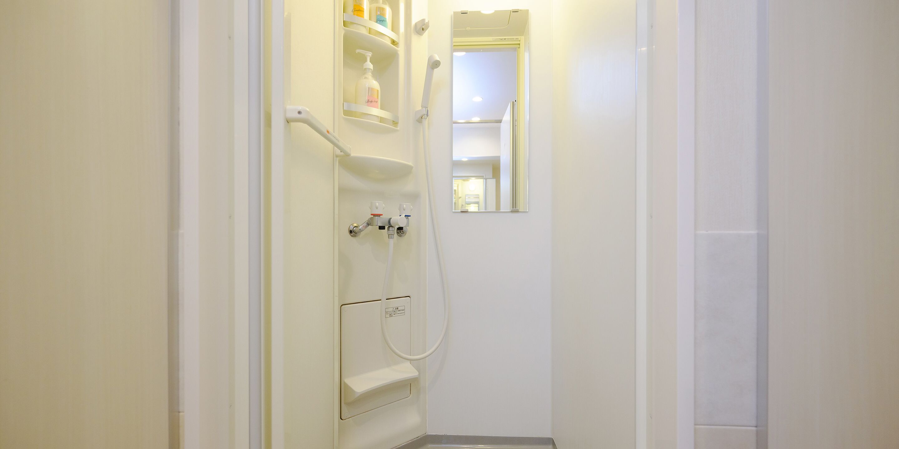 Un baño con ducha, espejo y estante con artículos de aseo.