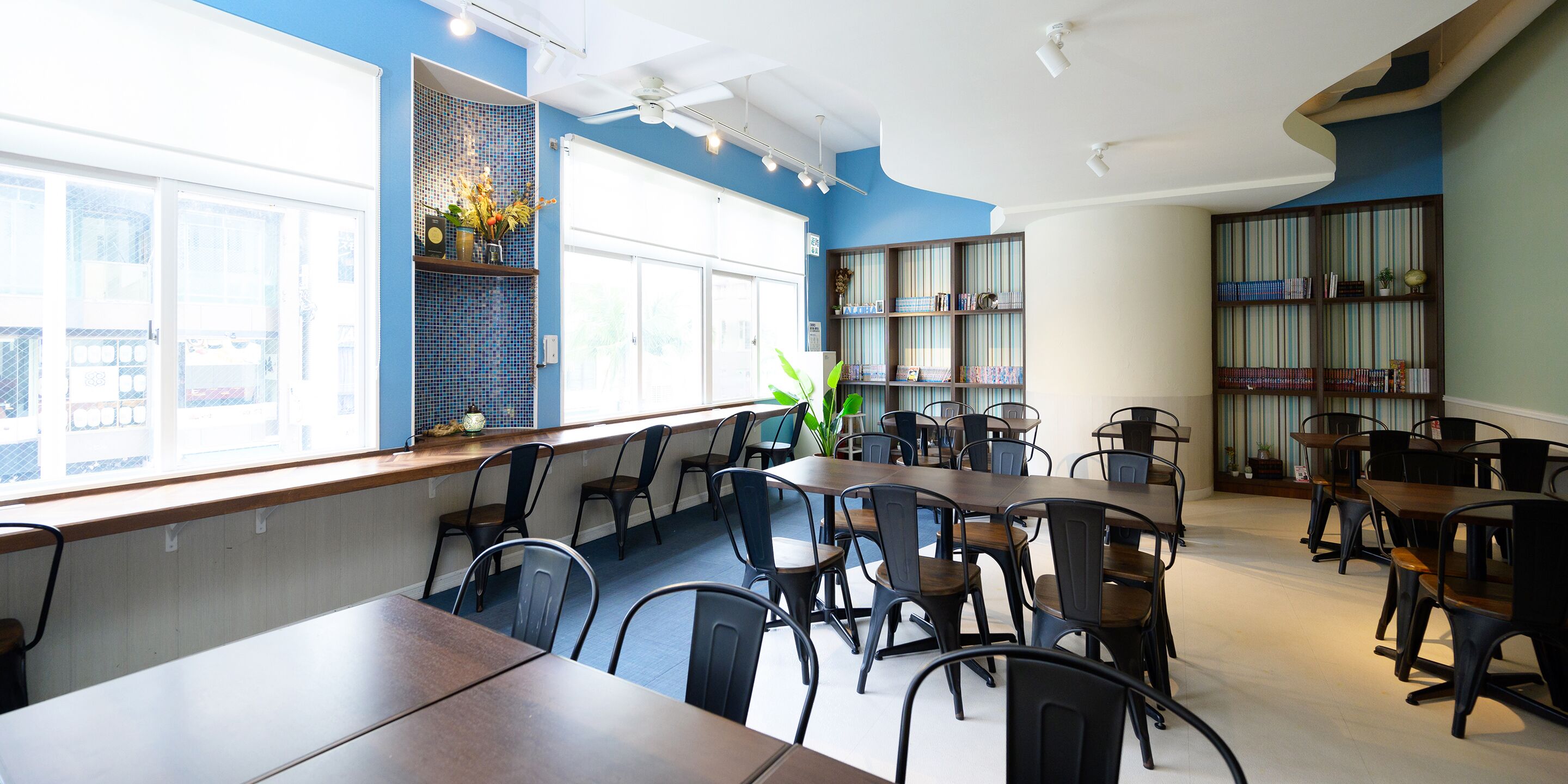 A dining area with multiple tables and chairs, a large window with a view, and a bookshelf with striped patterns.