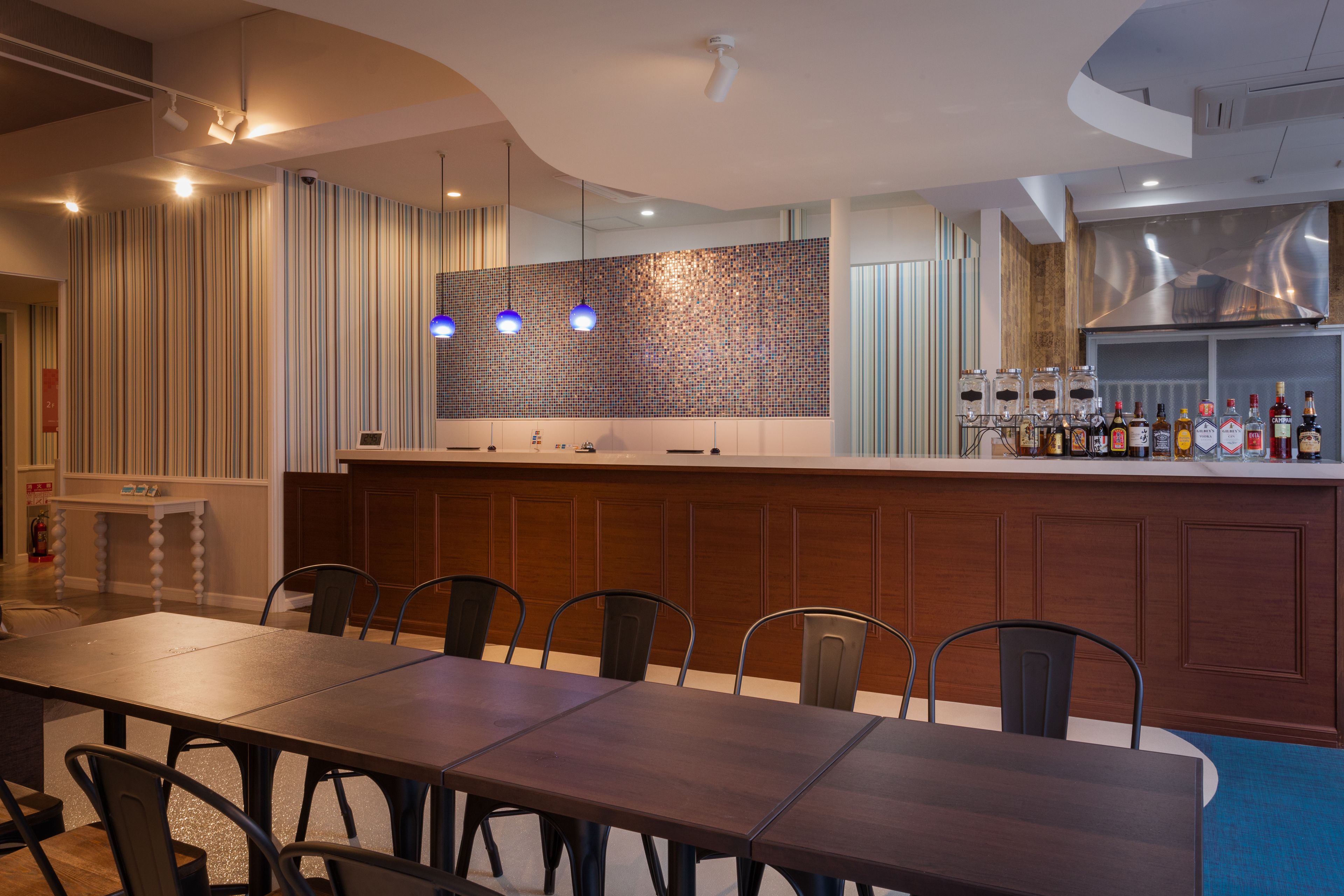 Un'area pranzo moderna con un tavolo lungo e sedie, un bancone cucina con sgabelli e un rivestimento decorativo.