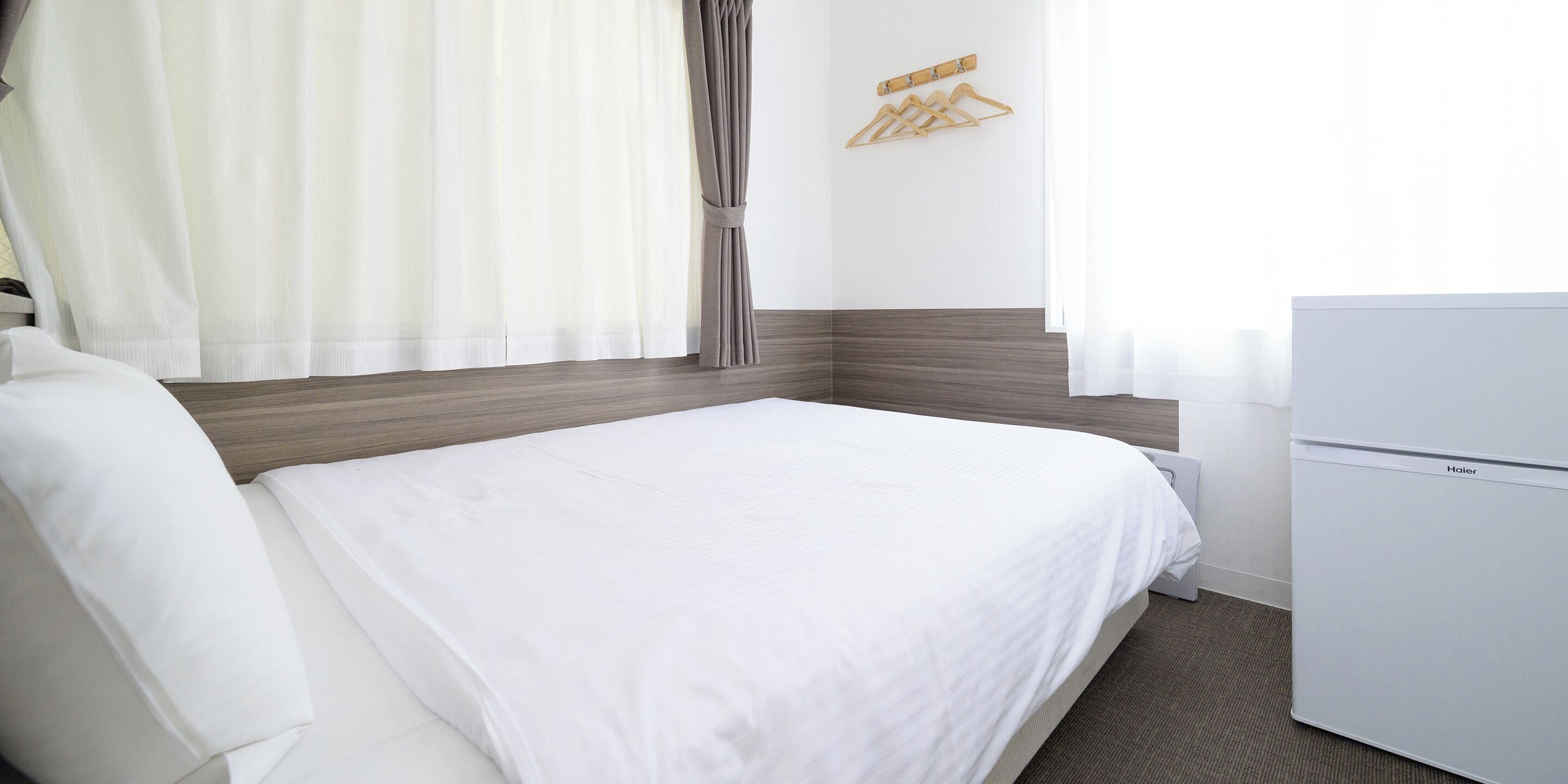 Ein Hotelzimmer mit einem Bett, einer weißen Kommode, einem Wandhaken für Kleidung und einem Fenster mit Vorhängen.