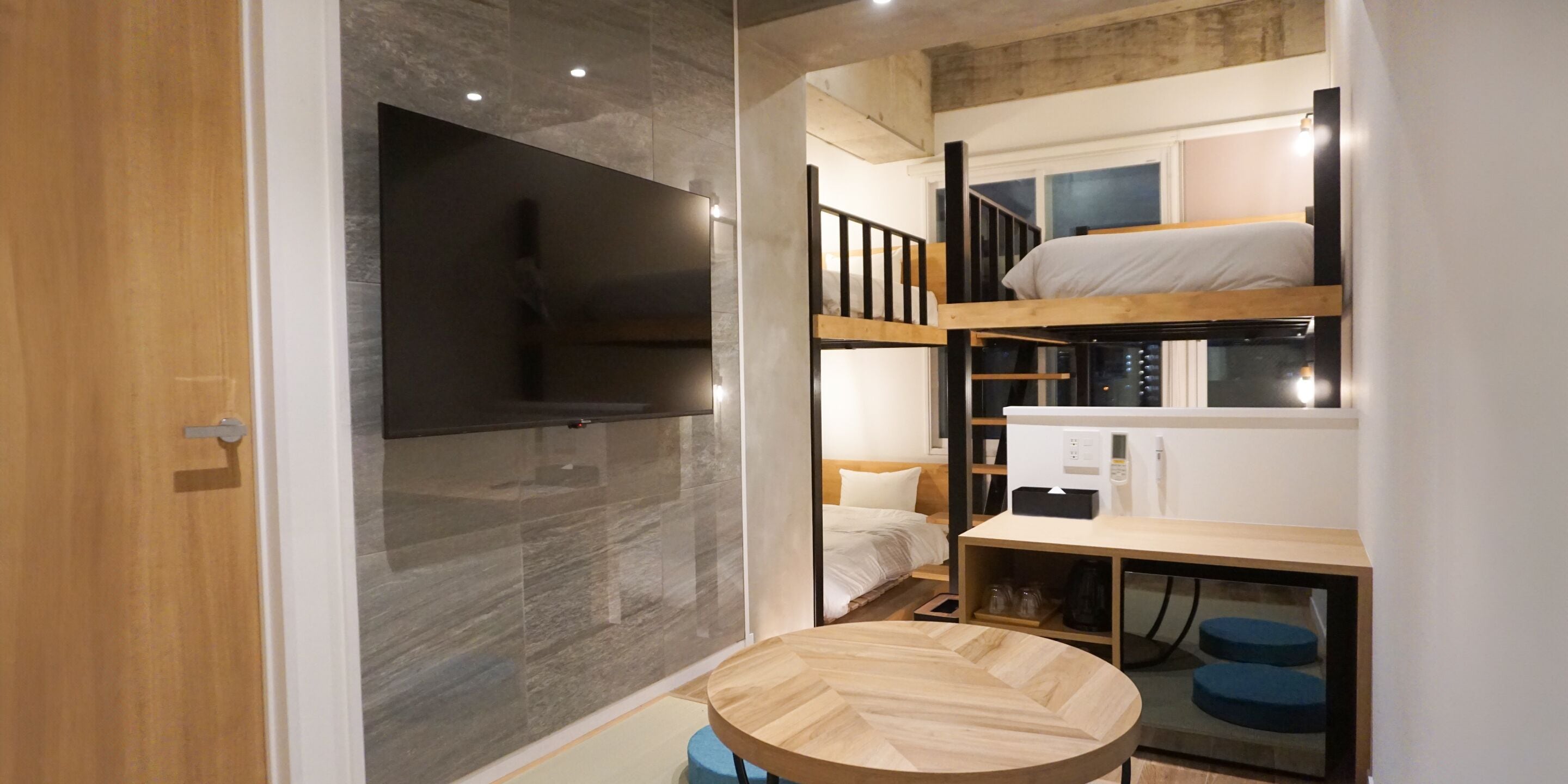 A compact room with a bunk bed, a small desk, and a television mounted on the wall.