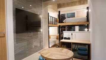 A compact room with a bunk bed, a small desk, and a television mounted on the wall.