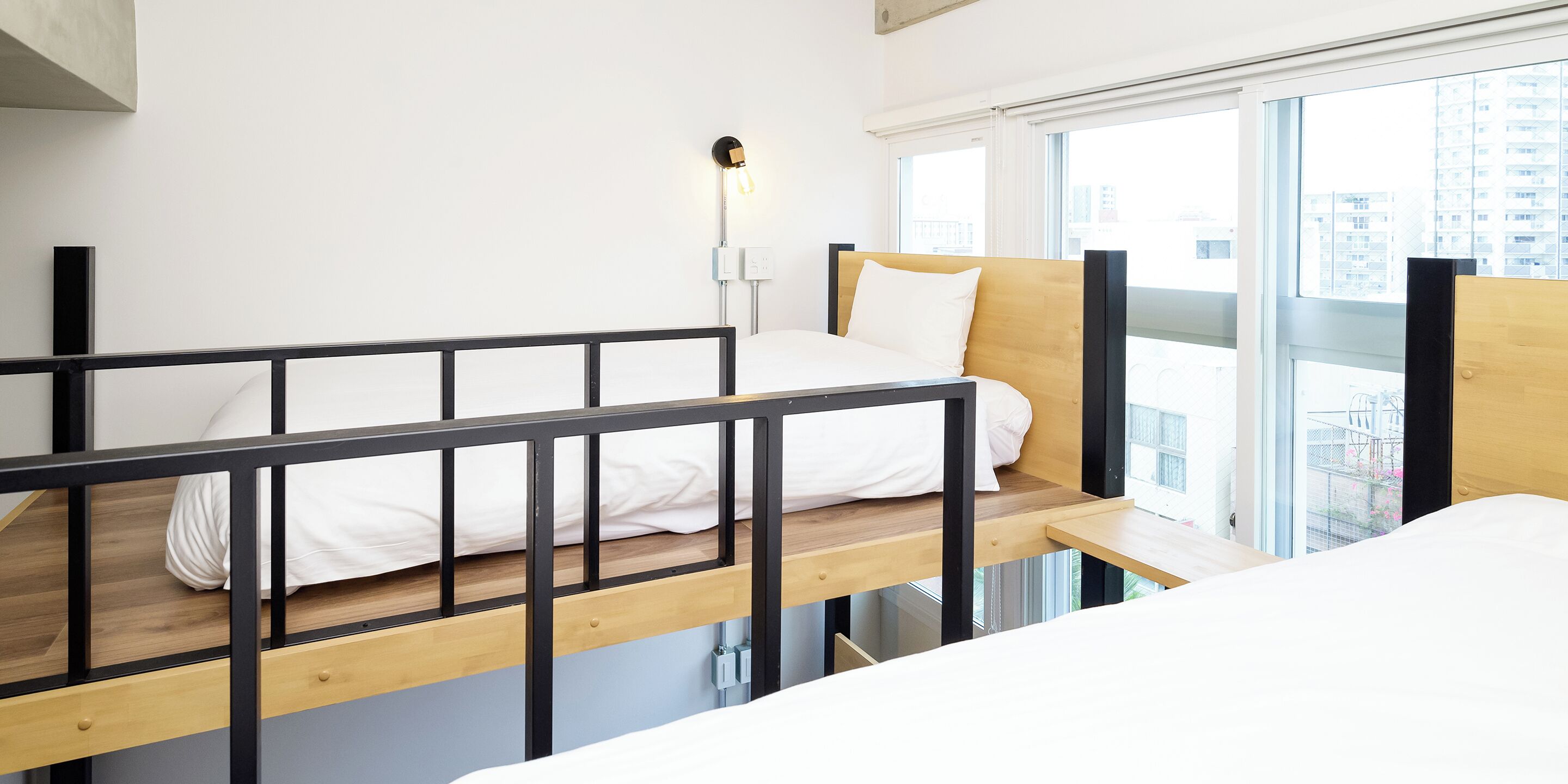 Une chambre d’hôtel moderne avec un lit superposé, une table de chevet et une grande fenêtre donnant sur la ville.