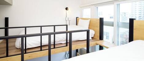 Une chambre d’hôtel moderne avec un lit superposé, une table de chevet et une grande fenêtre donnant sur la ville.