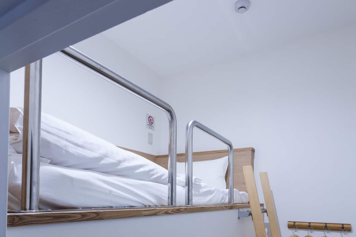 A bunk bed with a wooden ladder and a metal railing, a wall-mounted clothes rack, and a no-smoking sign.