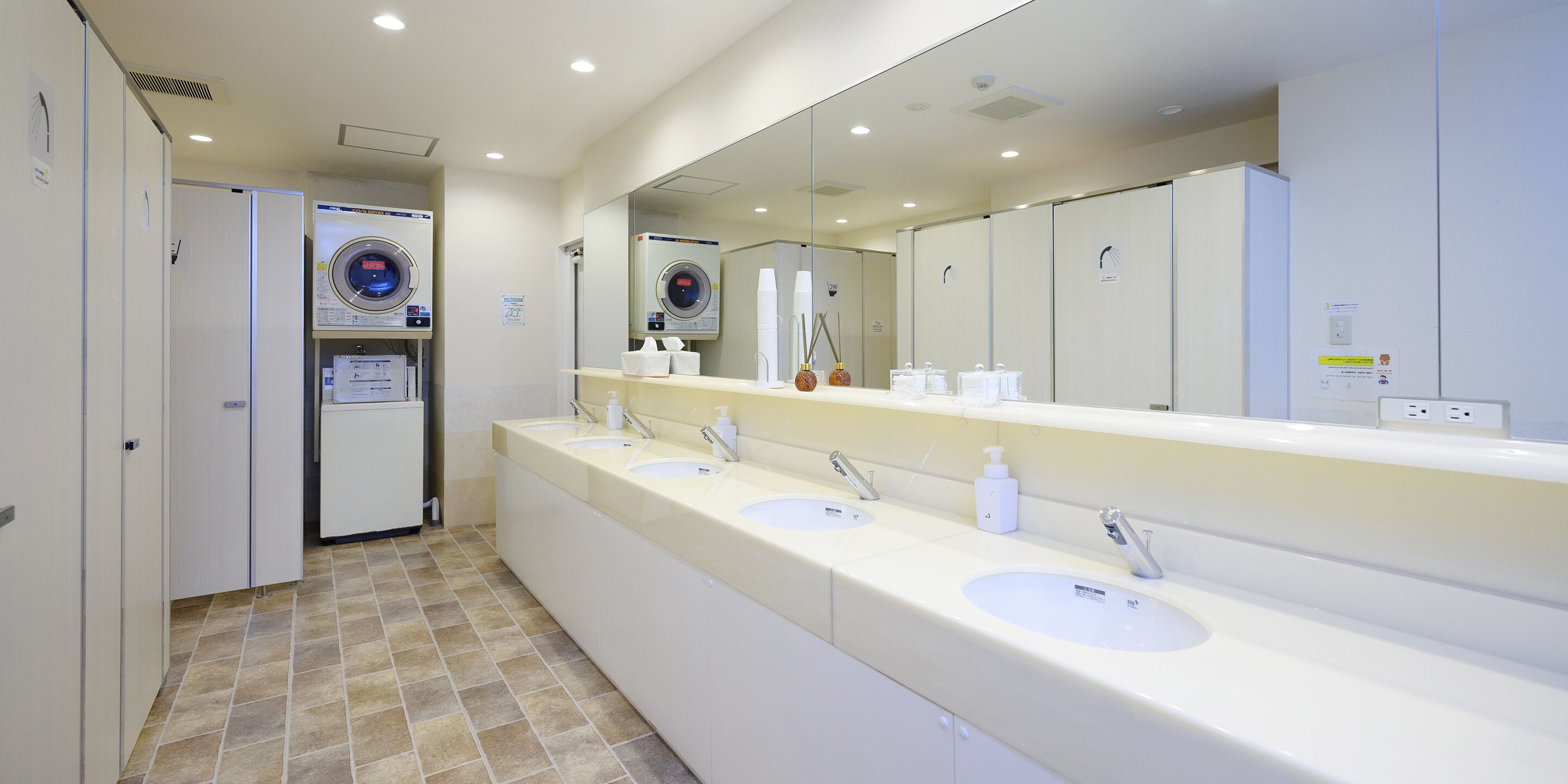 Un baño de hotel con un tocador largo, varios lavamanos, un espejo grande y una lavadora.