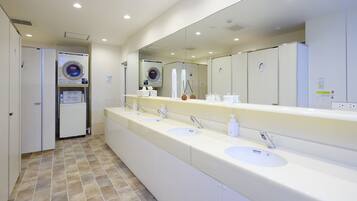 A hotel bathroom with a long vanity, multiple sinks, a large mirror, and a washing machine.