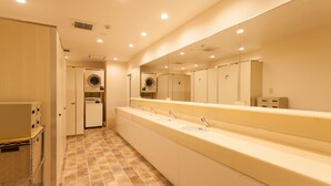 Un baño público con un mostrador largo, varios lavamanos, un espejo grande y una lavadora.