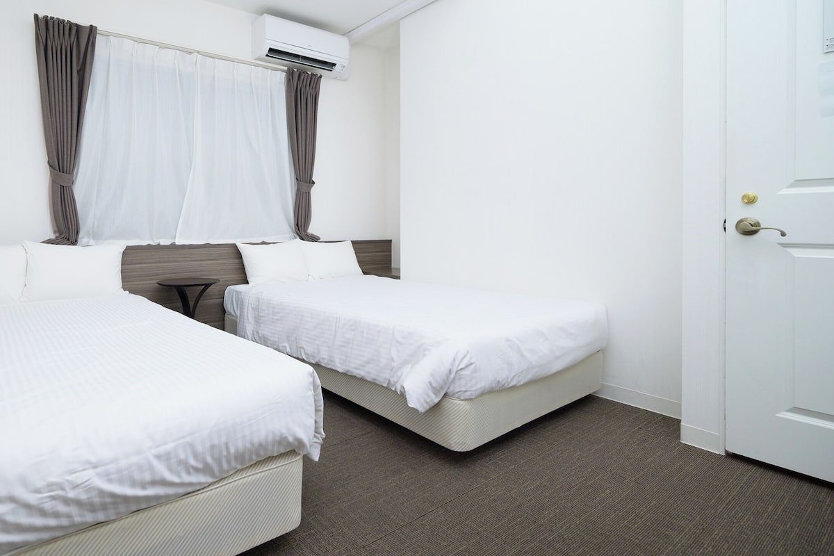 A hotel room with two single beds, a small table, and a window with curtains.