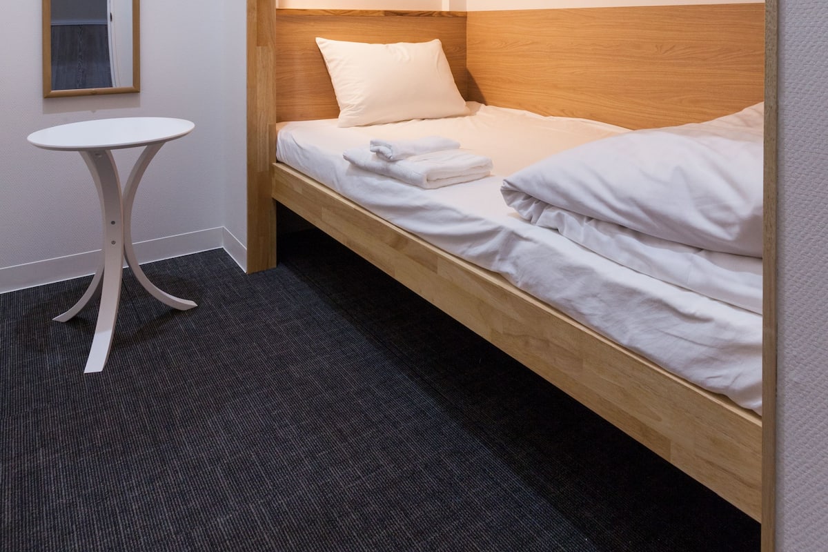A single bed with a wooden headboard, a small round table, and a mirror on the wall.