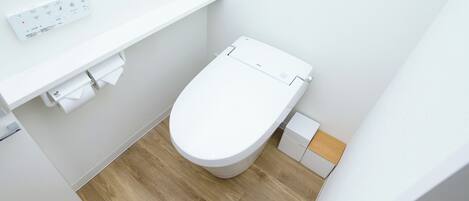 A small, modern bathroom with a white toilet, a toilet paper holder, and a small trash bin.