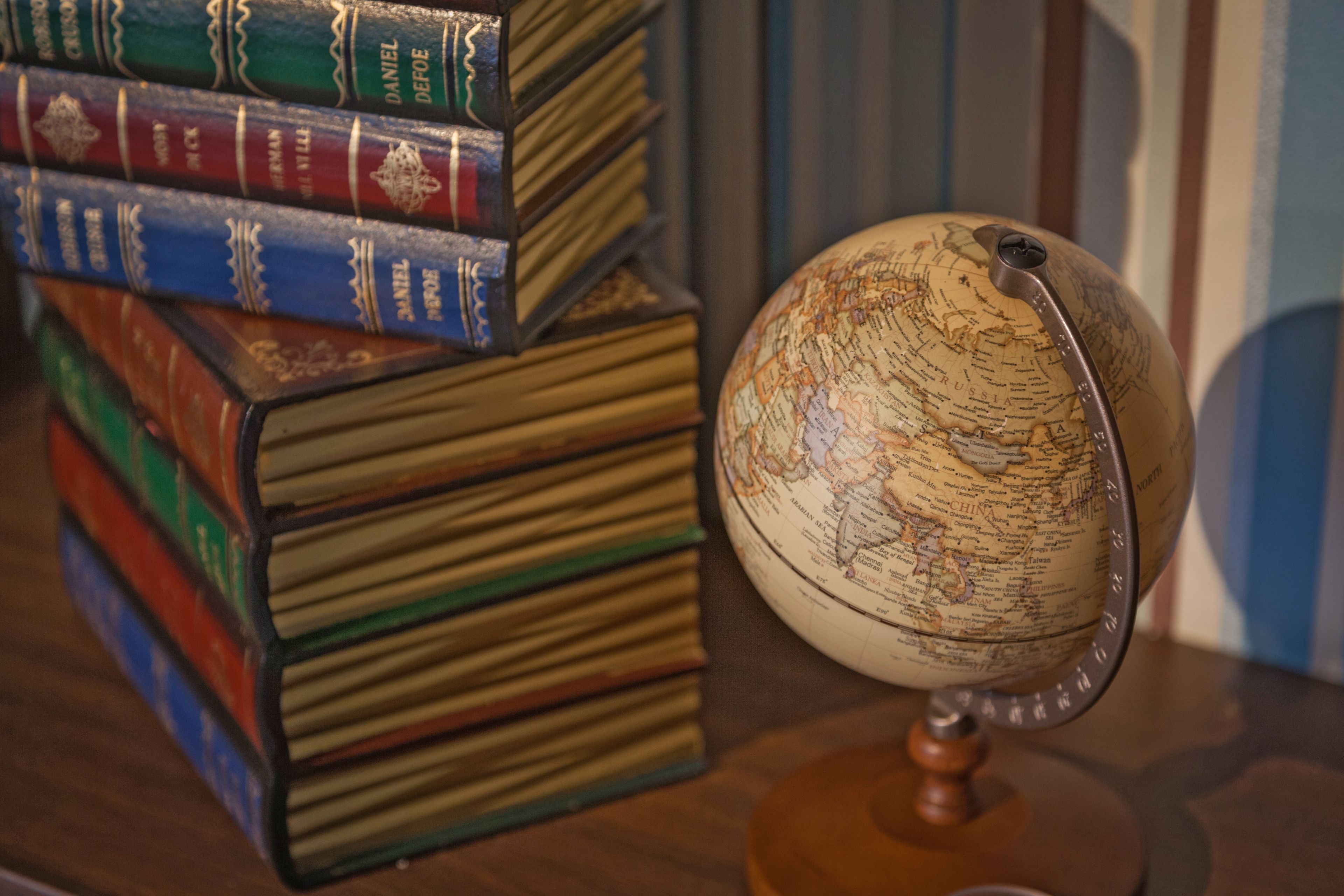 A globe on a stand with a stack of books behind it.