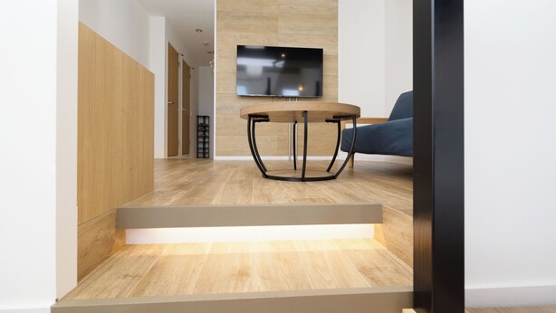 Una sala de estar moderna con suelo de madera, una mesa redonda con base de metal negro y un sofá azul.