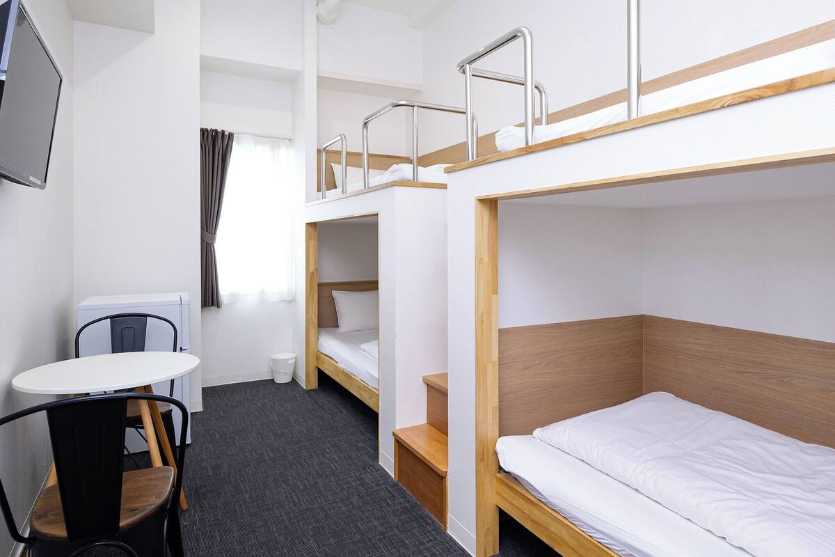 A bunk bed room with a small table and chair, a desk, and a window with curtains.