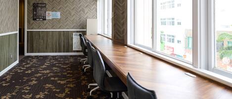 Un salón de conferencias con una larga mesa, sillas, una alfombra estampada con motivos florales y un ventanal con vistas a edificios.
