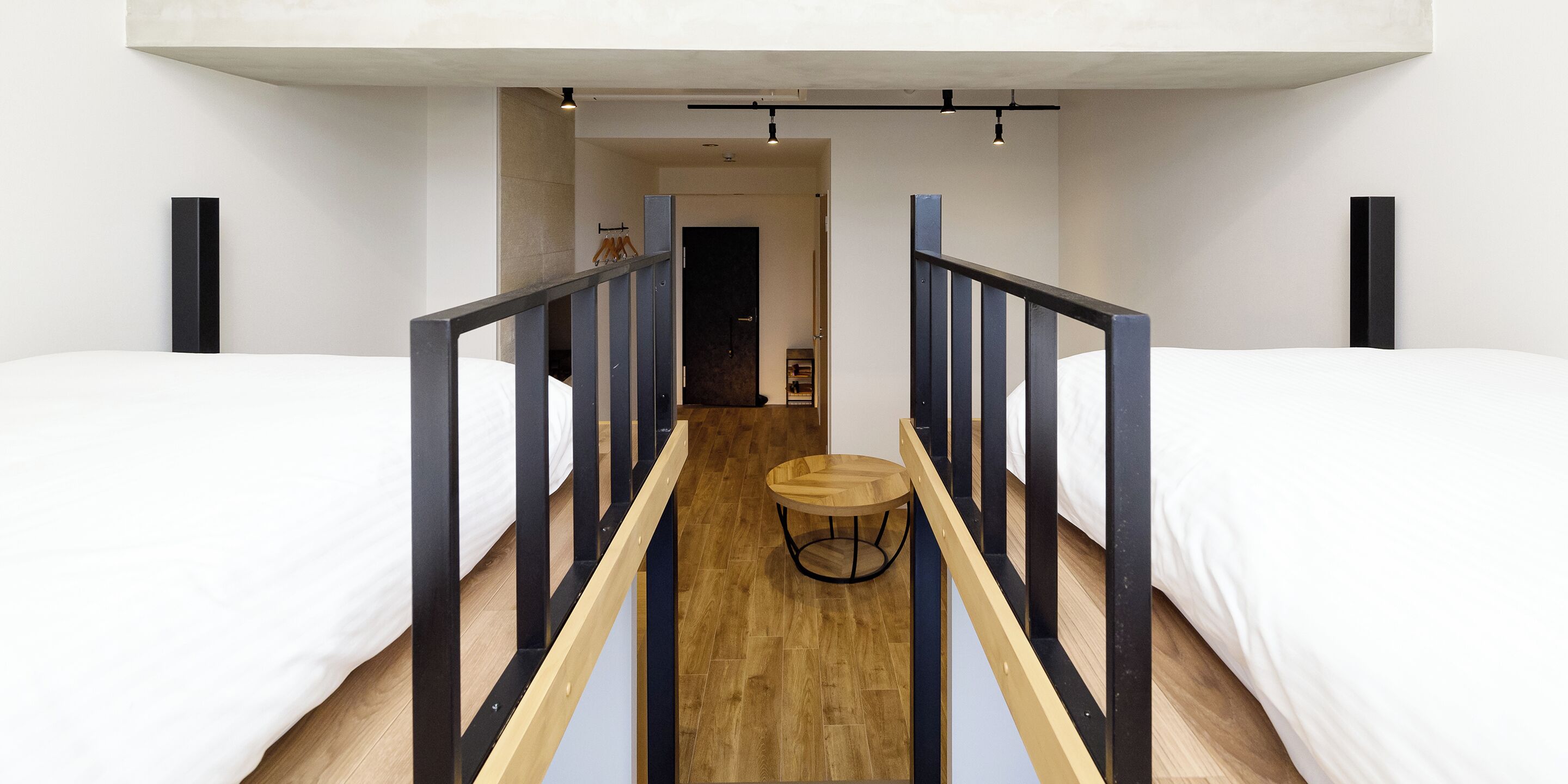A modern hotel room with two beds, a wooden floor, and a central round table.