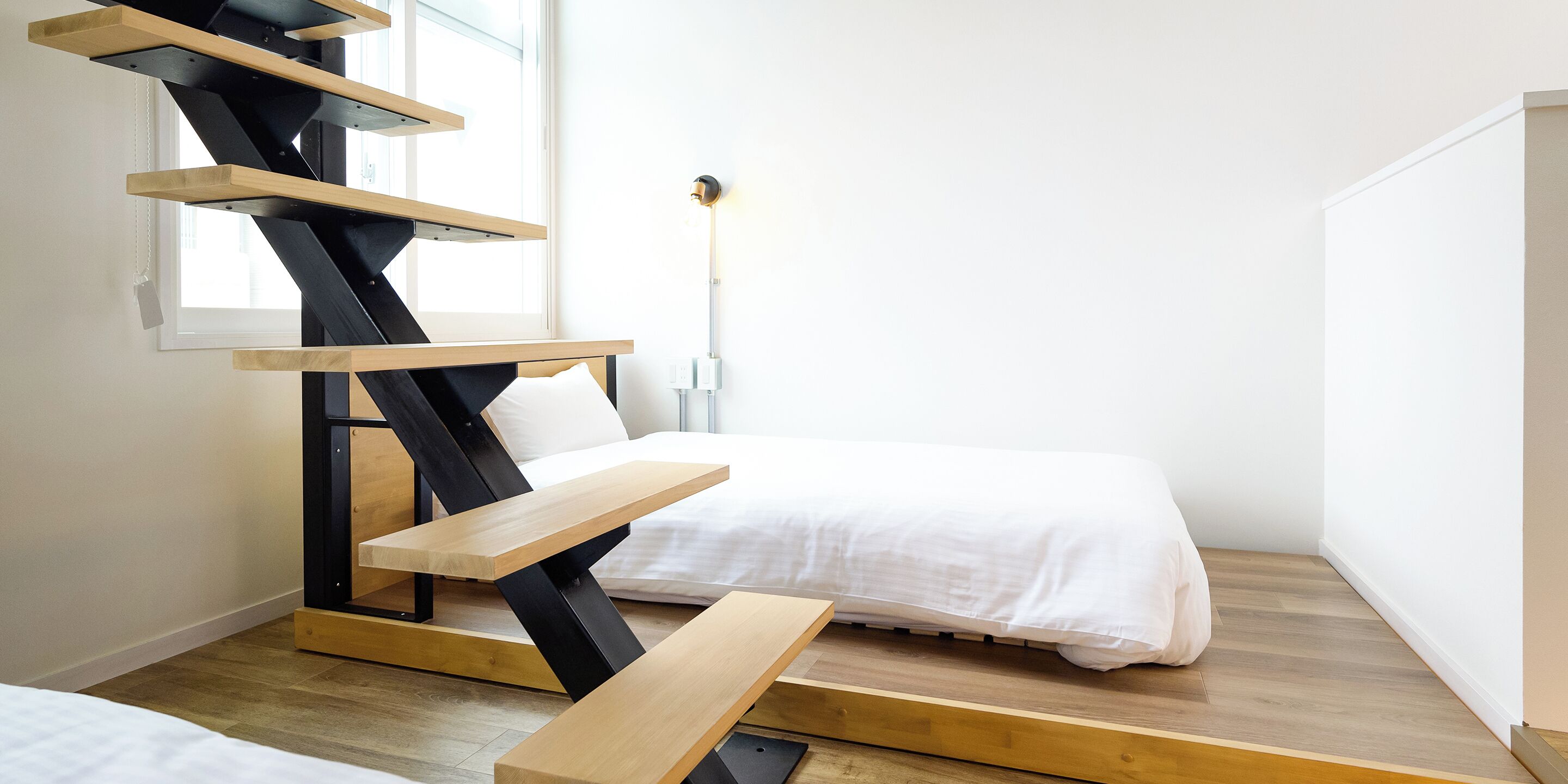 A modern room with a bed, a wooden desk, and a unique black and wooden staircase.