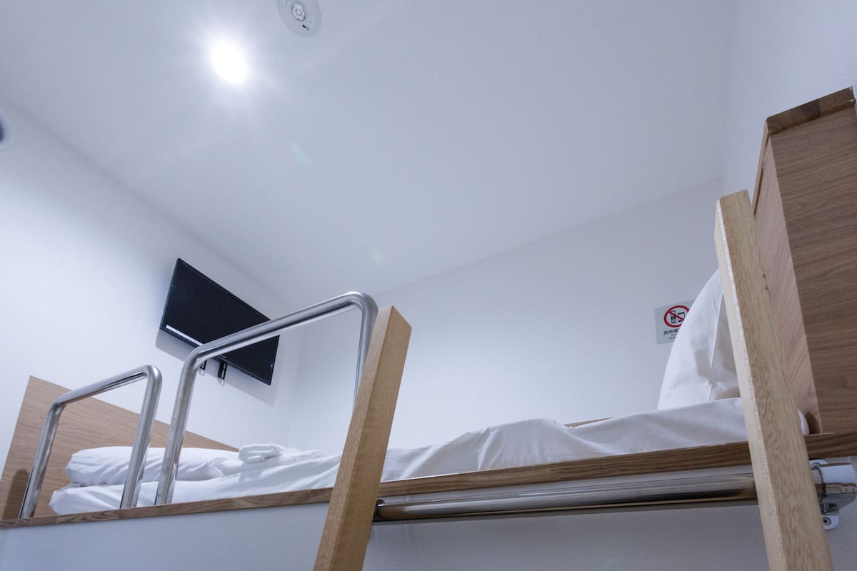 A bunk bed with metal railings, a television mounted on the wall, and a no-smoking sign.
