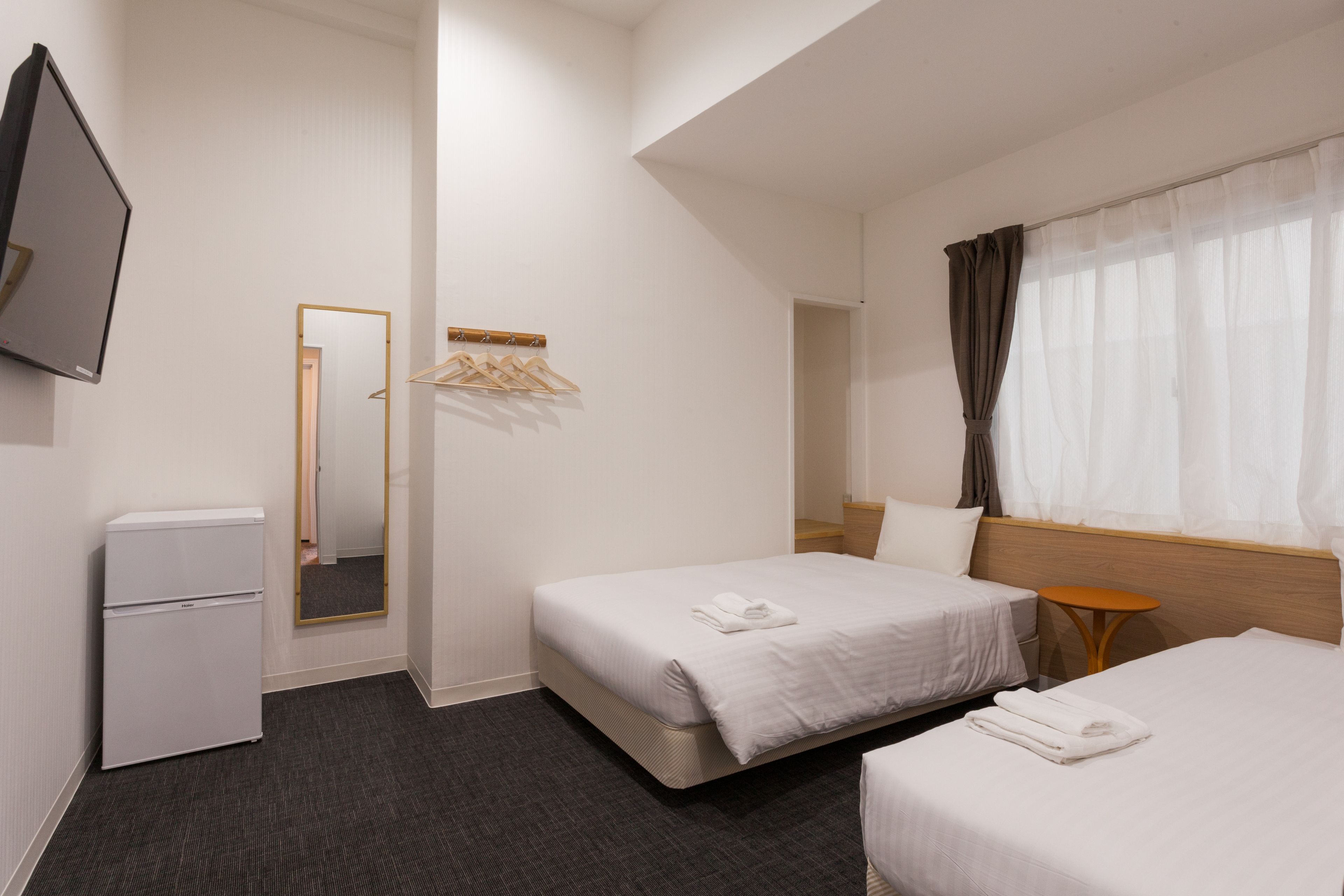 Una habitación de hotel con dos camas, un escritorio pequeño, un espejo y una televisión.