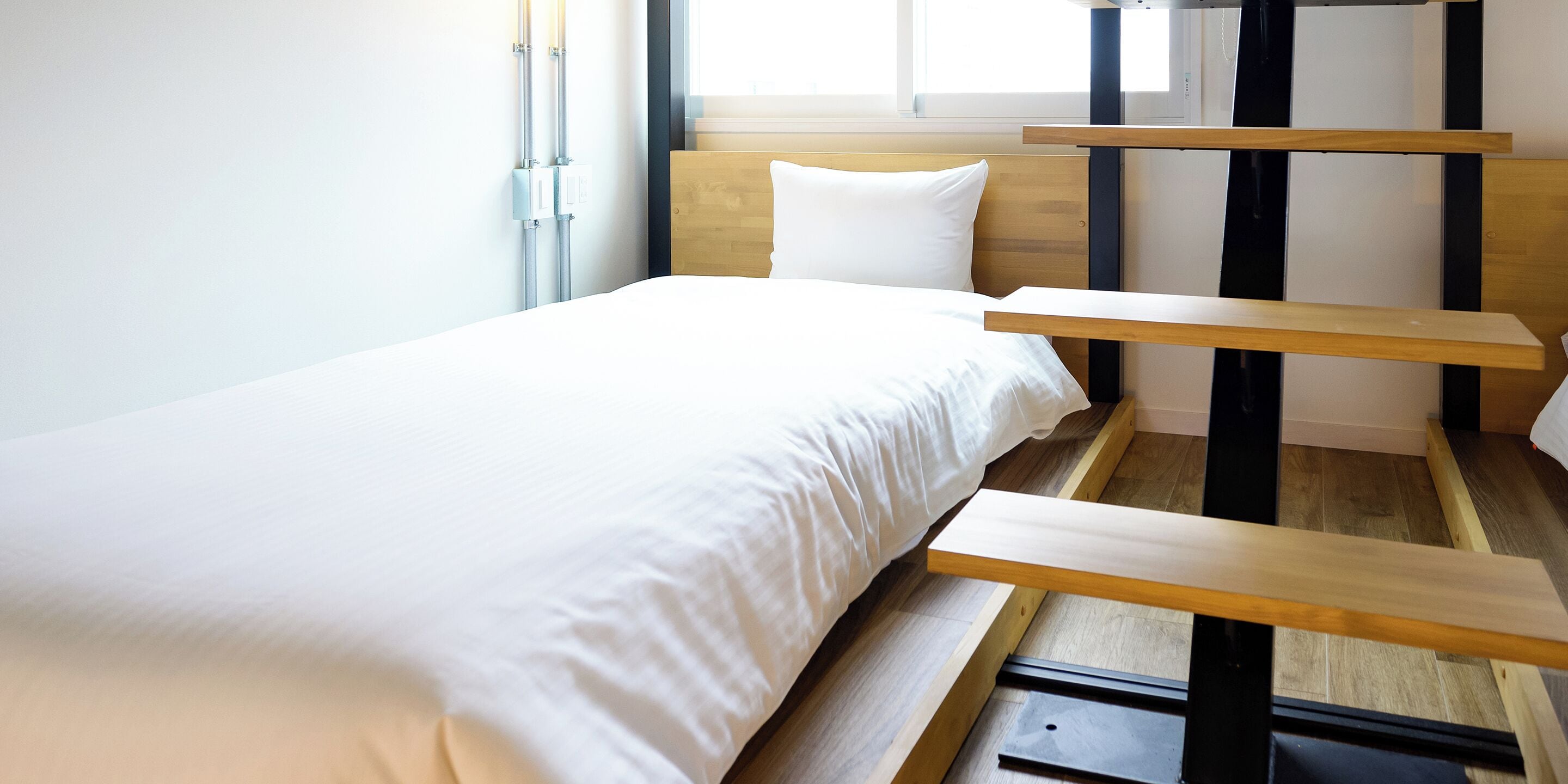 Une chambre au décor minimaliste, avec un lit, une tête de lit en bois et une fenêtre équipée de stores.