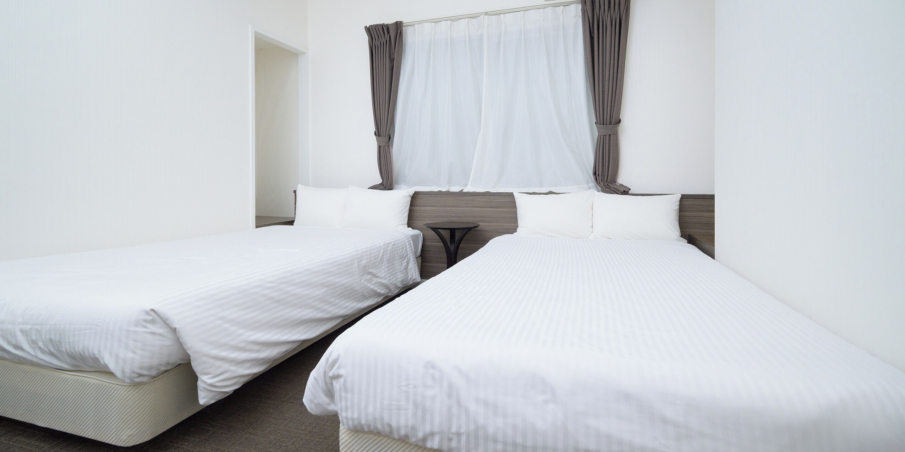 Zwei Betten mit weißer Bettwäsche in einem Hotelzimmer.