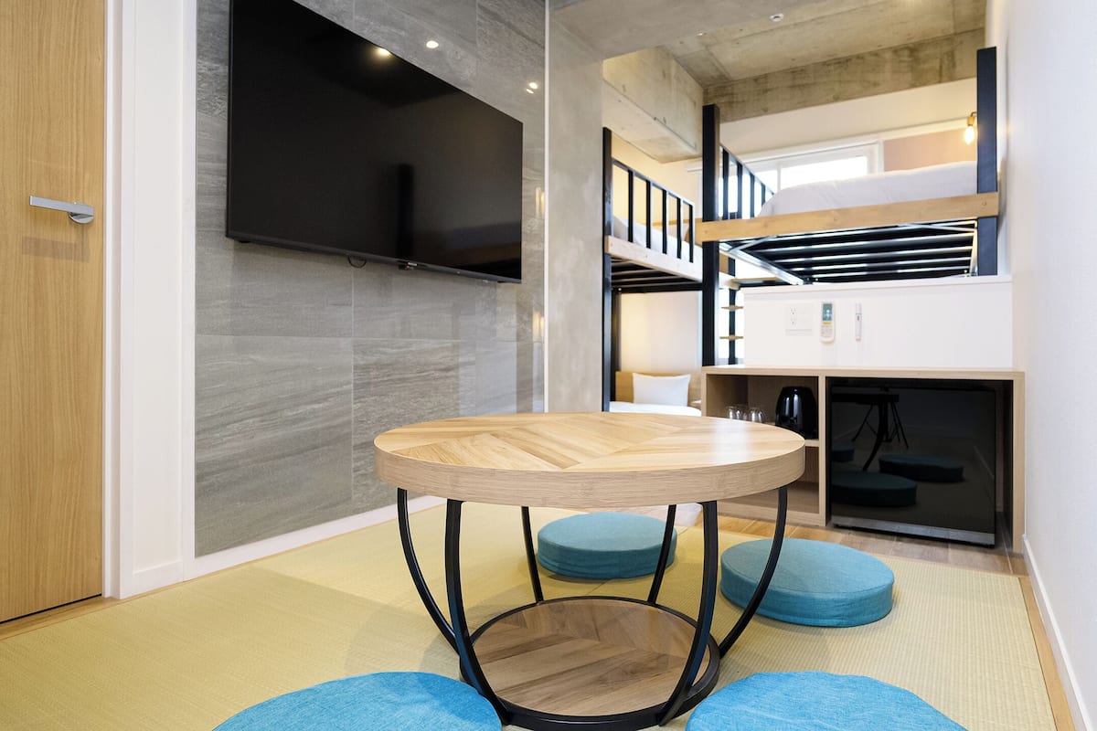 A modern interior with a round table, blue cushioned seating, a TV mounted on the wall, and a staircase leading to an upper level.