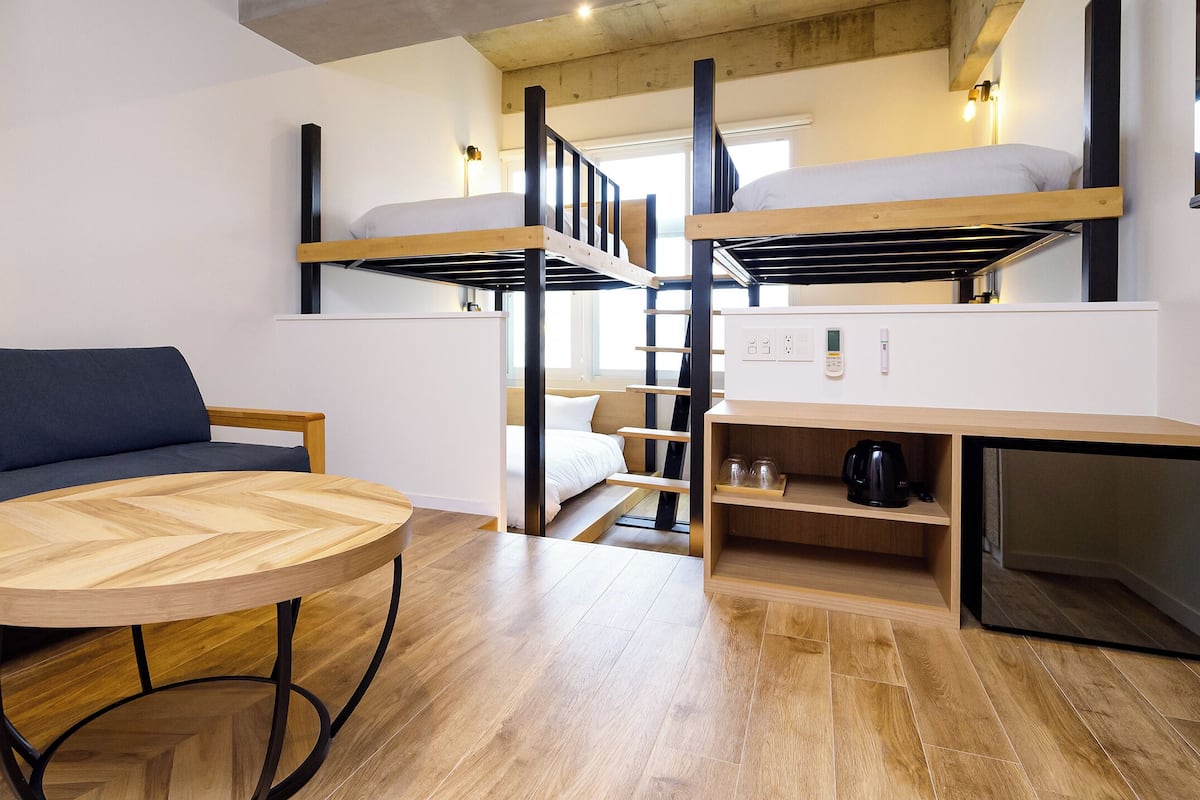 A compact room with bunk beds, a sofa, a round wooden table, and a small kitchenette.