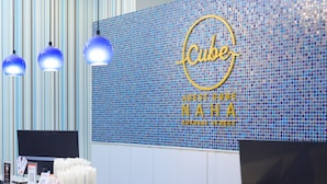 Zona de recepción de un hotel con una pared de mosaico azul, un cartel que dice 'Cube' y tres lámparas colgantes.