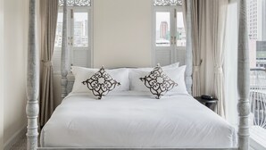 Un lit à baldaquin avec des poteaux aux quatre coins, un ciel de lit blanc, un coussin à motifs et une table de chevet.