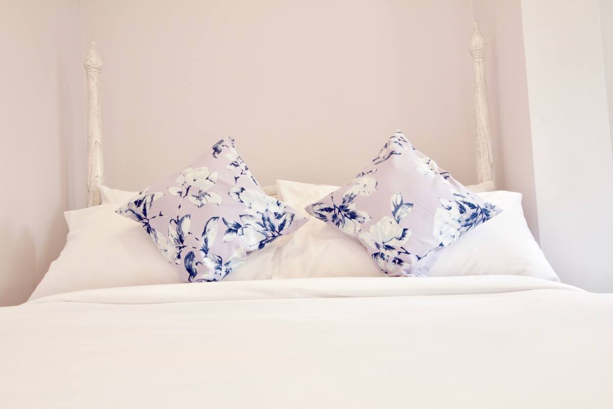Un lit avec une literie blanche et deux coussins à motifs floraux.